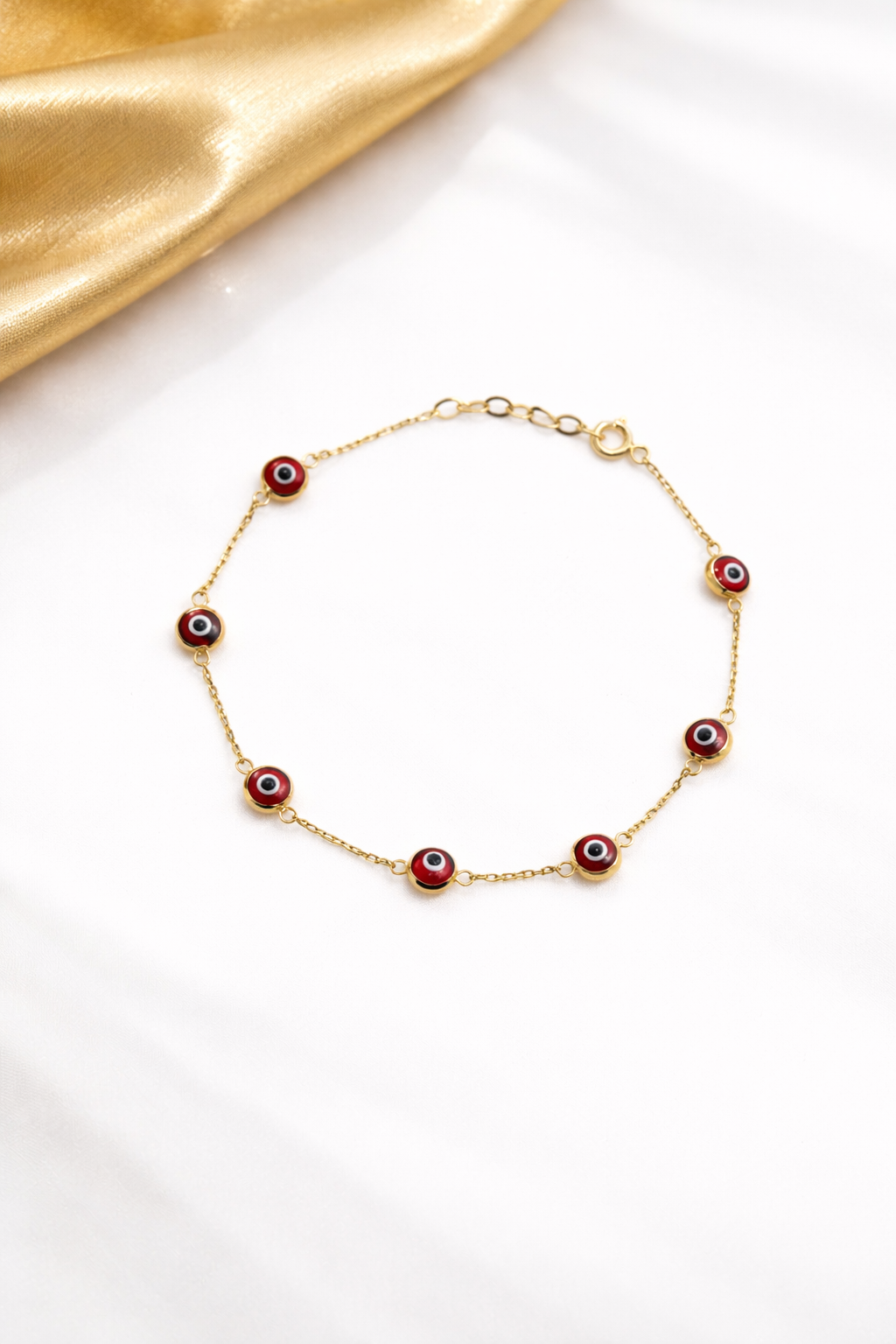 Gold bracelet with red evil eye charms on a white background