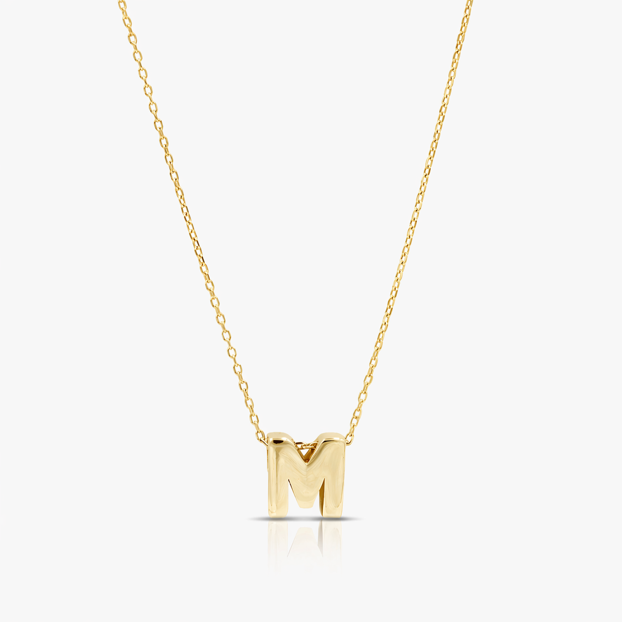 Gold necklace with a 'M' pendant on a light gray background