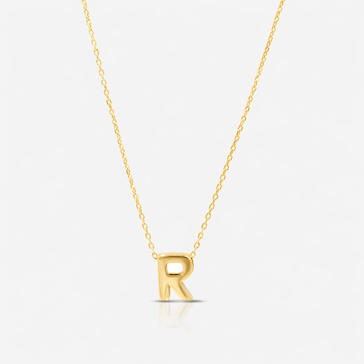 Gold necklace with a 'R' pendant on a light gray background