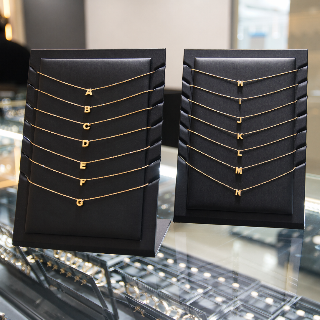 Two black display stands with gold necklaces labeled A to N on a reflective surface.